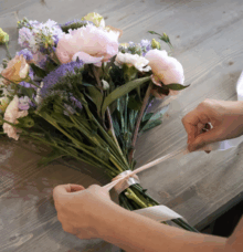 En person binder en bukett med blommor på ett träbord.